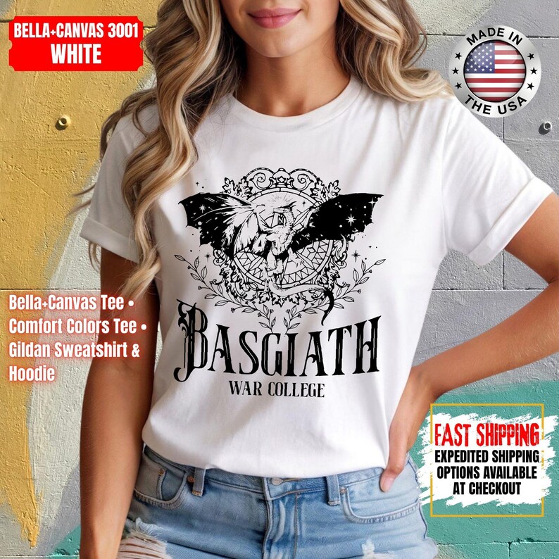 Op de afbeelding: Wit T-shirt met een zwarte afbeelding van een gevleugeld wezen in een decoratief kader, met de tekst "BASGIATH WAR COLLEGE" eronder. Het shirt is gelabeld met "BELLA+CANVAS 3001 WHITE" en "MADE IN THE USA".