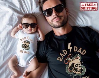 May include: A black t-shirt and a white baby onesie with matching graphics. The t-shirt and onesie feature a skull with a snake, lightning bolt, and the words "RAD DAD SOCIETY" and "RAD LIKE MY DAD". Both are wearing sunglasses.