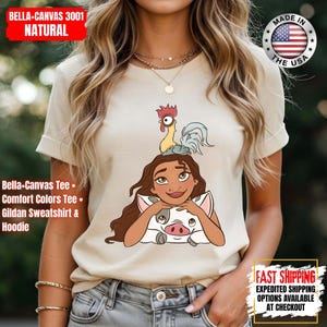 May include: Natural-colored Bella+Canvas 3001 t-shirt featuring a cartoon illustration of a character with long brown hair, a pig, and a rooster. The shirt has rolled-up sleeves. Text on the shirt includes "Bella-Canvas Tee" and "Comfort Colors Tee."