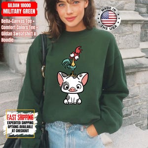 K&ouml;nnte beinhalten: Milit&auml;rgr&uuml;nes Gildan-Sweatshirt mit einem Cartoon-Schwein- und Hahn-Design. Das Sweatshirt tr&auml;gt den Text "GILDAN 18000 MILITARY GREEN" und "MADE IN THE USA" auf dem Bild.