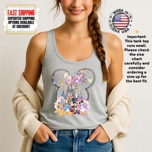 May include: A light gray tank top featuring a Minnie Mouse design. The design includes a pink bow, a castle, and various Disney characters. The text "Important: This tank top runs small. Please check the size chart carefully and consider ordering a size up for the best fit." is also visible.