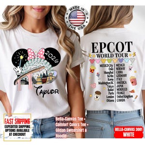 May include: White t-shirt featuring a colorful graphic of a theme park with a Minnie Mouse bow and the text "2026 Taylor". The back of the shirt displays "EPCOT WORLD TOUR" and a list of cities. Made in the USA.
