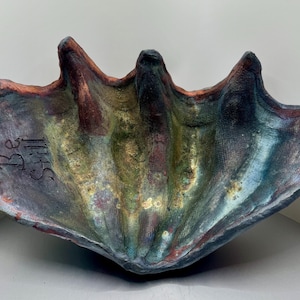 May include: A ceramic clam shell with a blue, green, and brown glaze. The shell has the words "Be Still" inscribed on the inside.