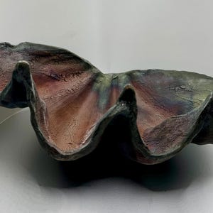 May include: A ceramic bowl shaped like a seashell with a dark green, brown, and red glaze.