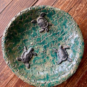 May include: A green ceramic bowl with a net-like pattern and three black turtle figurines. The bowl is perfect for serving snacks or holding trinkets.