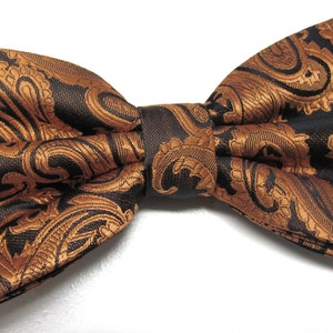 May include: A black and gold paisley patterned bow tie. The bow tie is made of a soft, silky fabric.