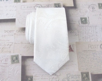 Puede incluir: Corbata blanca con estampado de paisley. La corbata está hecha de un tejido texturizado y tiene un brillo sutil.