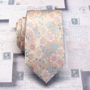 May include: A beige necktie with a floral pattern in pink and light blue. The tie is made of a shiny fabric and is folded over itself. The background includes vintage postcards.