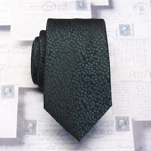 May include: A dark green tie featuring a repeating leaf design. The tie is made from a textured material and is shown against a backdrop of vintage postcards.