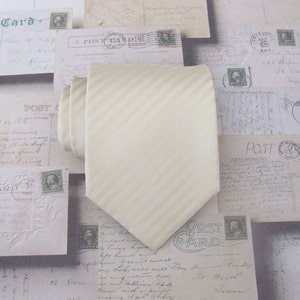 May include: A cream-colored striped tie with a satin finish. The tie is made of a soft, smooth fabric and has a subtle sheen.