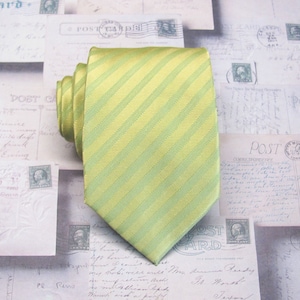 May include: A yellow and green striped silk necktie. The tie is folded and lying on a surface with old postcards.