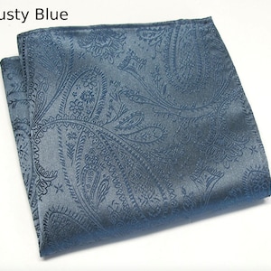 May include: A folded dusty blue paisley pocket square. The fabric has a subtle sheen and a detailed, repeating pattern. The text "Dusty Blue" is in the upper left corner. This accessory is suitable for formal wear.
