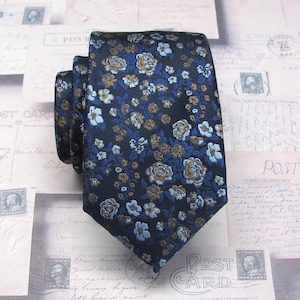 Peut inclure: Une cravate bleu marine ornée d'un motif floral dans des tons de bleu et de beige. Le tissu texturé de la cravate est noué, mettant en valeur le design. Le fond présente des cartes postales vintage.