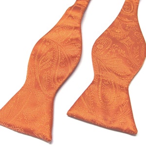 Pode incluir: Uma gravata borboleta laranja com padrão paisley. A gravata borboleta é feita de um tecido macio e sedoso com um brilho sutil.