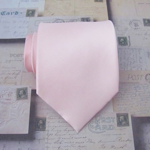 Può includere: Una cravatta di raso rosa chiaro. La cravatta è di un solo colore senza motivo.