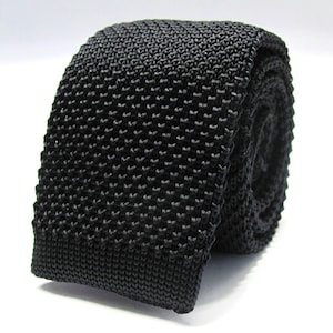 May include: A black knitted tie with a textured pattern. The tie is rolled up and ready to be worn.