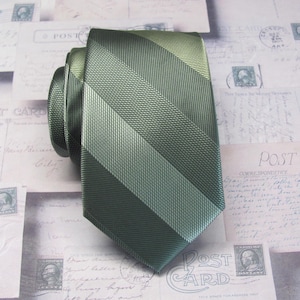 Puede incluir: Una corbata de rayas verdes y verde claro con un patrón diagonal. La corbata está hecha de un material sedoso.