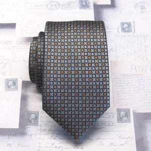 May include: A patterned necktie in shades of gray, black, and orange. The tie features a repeating geometric design of small squares and crosses. The tie is made of a smooth fabric and is neatly folded.