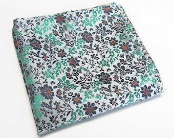 May include: A white pocket square with a floral pattern in shades of green, blue, and orange.