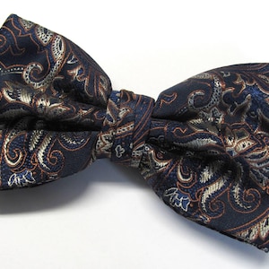 May include: A navy blue bow tie with a paisley pattern in shades of gold, brown, and blue.