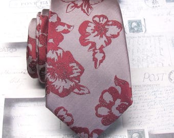 May include: A rolled-up tie with a floral pattern. The tie is a light gray color with large, red flowers. The tie is made of a smooth fabric and is suitable for formal occasions.