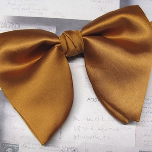 Puede incluir: Una pajarita de satén dorada. La pajarita está atada y lista para usar.