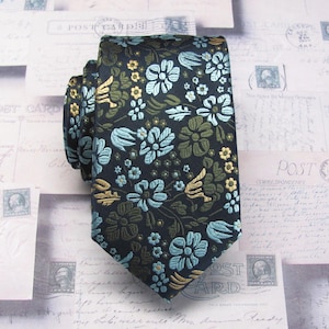Peut inclure: Une cravate présentant un fond noir foncé avec un motif floral complexe dans des tons bleu clair, vert olive et doré. Le design se compose de diverses formes de fleurs et de feuilles réparties sur le tissu selon un motif répétitif.