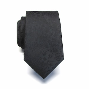 May include: A black tie with a delicate floral design. The tie is made of a smooth material and is rolled up, highlighting its texture and pattern. A classic accessory for formal or business wear.