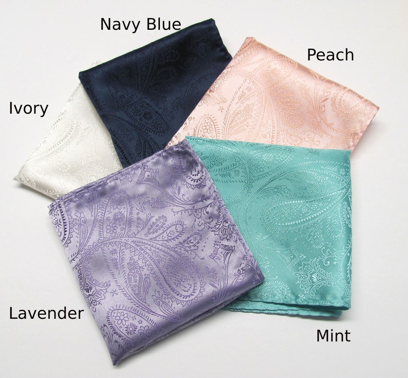 May include: A selection of folded paisley pocket squares in colours such as ivory, navy blue, peach, mint, and lavender. The fabric has a slight sheen, and the paisley pattern is visible.