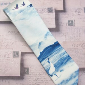 May include: A blue and white silk tie with a watercolor design of birds flying over a mountain range and a crane standing in a body of water.