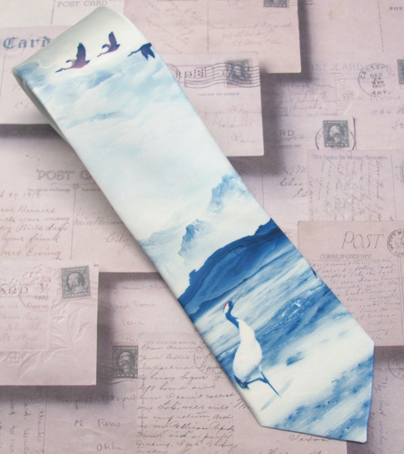 May include: A blue and white silk tie with a watercolor design of birds flying over a mountain range and a crane standing in a body of water.