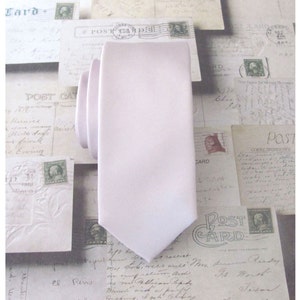 Könnte beinhalten: Eine hellrosa Satin-Krawatte. Die Krawatte ist einfarbig und hat eine spitze Spitze.