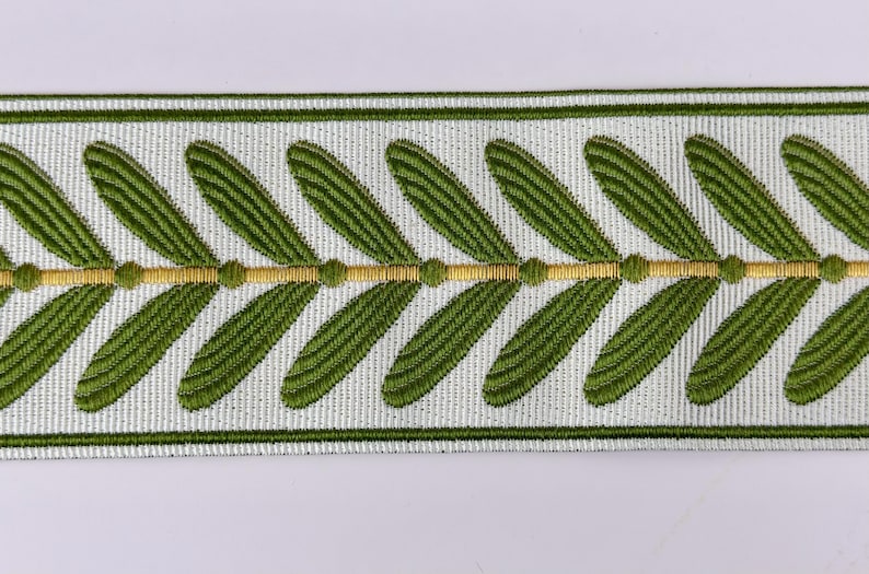 May include: Decorative trim featuring a repeating pattern of green leaves on a white background. A gold-colored line with small dots runs through the center of the design. The trim is bordered by thin green lines.