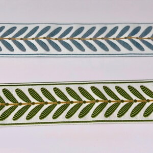 May include: Two decorative ribbons with leaf patterns. One ribbon is white with blue leaves and gold accents. The other ribbon is white with green leaves and gold accents. Both ribbons have a repeating leaf design.