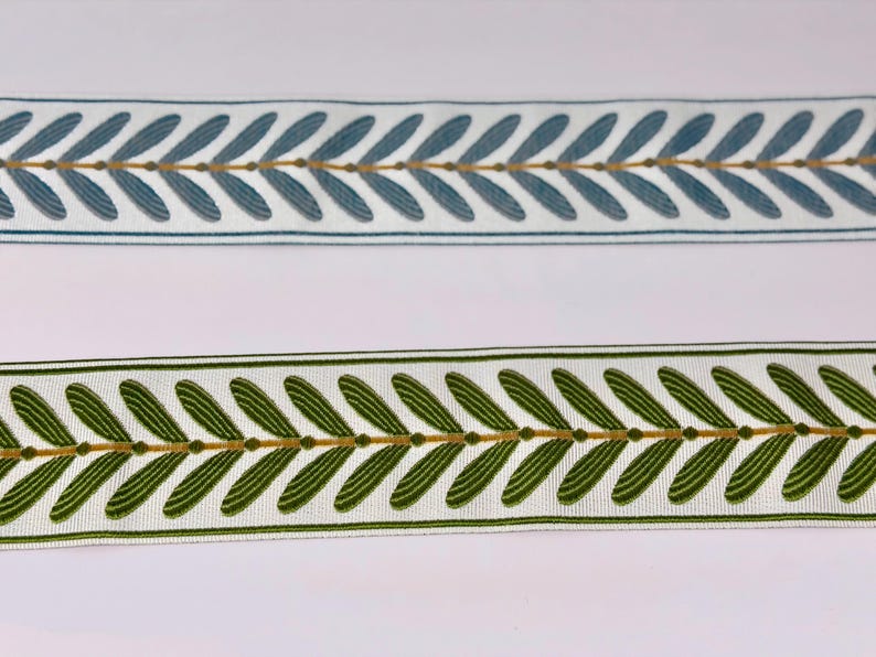 May include: Two decorative ribbons with leaf patterns. One ribbon is white with blue leaves and gold accents. The other ribbon is white with green leaves and gold accents. Both ribbons have a repeating leaf design.