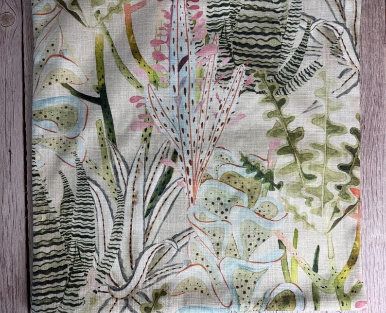 K&ouml;nnte beinhalten: Nahaufnahme eines Stoffes mit botanischem Druck. Das Design zeigt verschiedene Pflanzen in Gr&uuml;n-, Blau-, Rosa- und Beiget&ouml;nen. Der Stoff hat eine leinenartige Textur mit detaillierten und abstrakten Pflanzenillustrationen.