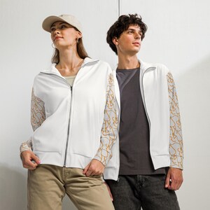 Puede incluir: Dos chaquetas deportivas blancas con cremallera, cuello alto y mangas largas con un patrón de líneas abstractas en gris claro y naranja. Las chaquetas tienen una cremallera plateada completa y puños acanalados en las muñecas.