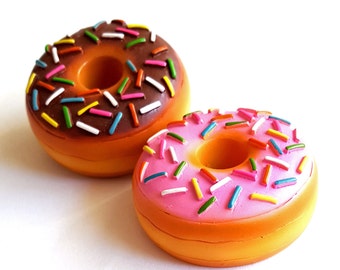 Puede incluir: Dos mini donuts con chispas de colores. Un donut tiene glaseado de chocolate y el otro tiene glaseado rosa.
