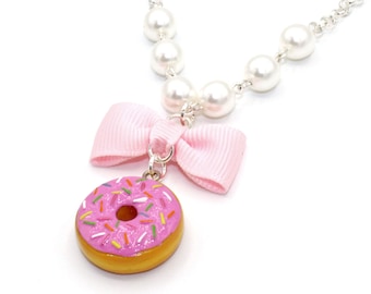 Könnte beinhalten: Eine Perlenkette mit einer rosa Schleife und einem rosa Donut mit bunten Streuseln.