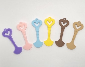 May include: Six colorful plastic key-shaped charms with heart-shaped cutouts. The charms are in shades of purple, pink, blue, yellow, brown, and beige.
