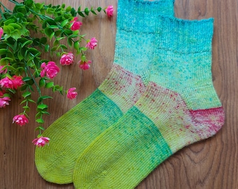 May include: A pair of hand-knitted socks featuring a variegated color palette of bright lime green, emerald green, and turquoise, with speckled accents of pink and orange throughout the fabric, including a ribbed cuff and a reinforced heel.