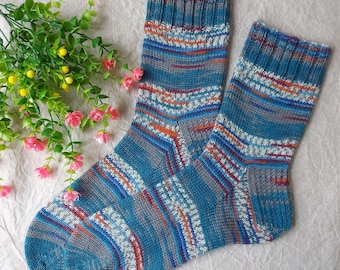 May include: A pair of hand-knitted socks featuring a variegated pattern of blue, grey, and orange yarn. The socks have a ribbed cuff at the top and a textured knit construction throughout, showcasing a multi-colored striped design.