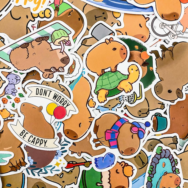 May include: A collection of colorful stickers featuring capybaras in various poses and settings. The stickers include phrases like "Don't Worry, Be Cappy" and depict capybaras riding turtles, wearing hats, and relaxing in nature.