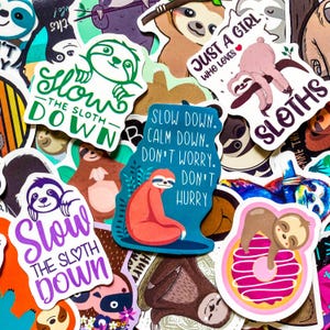 May include: A collection of colorful stickers featuring sloths in various poses. Some stickers have text like "Slow the Sloth Down" and "Just a Girl Who Loves Sloths." The stickers are in various shapes and sizes, with a variety of colors.