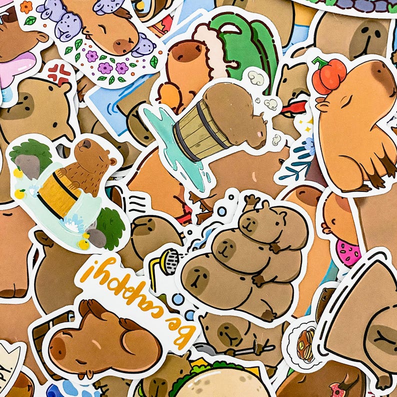 May include: A collection of colorful stickers featuring cartoon capybaras in various poses and activities. The stickers are printed on white paper and have a glossy finish. Some of the stickers feature the text "Be Capybara" and "ihohho".