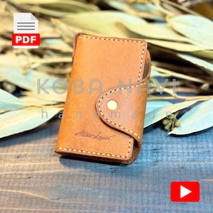 May include: A tan leather cardholder with a button clasp. The edges are stitched, and the text "KOBA NAVI handmade" and "Acee Laport" is visible. A PDF icon and a YouTube play button are also present in the image.