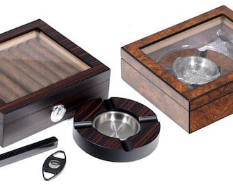 May include: A collection of cigar accessories, including two wooden humidors with glass tops, a round ashtray with a metal insert, a cigar cutter, and a cigar rest. The humidors are rectangular with a dark wood finish.