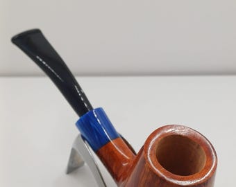 May include: A wooden tobacco pipe with a brown bowl and a black stem. The pipe has a blue and orange accent near the stem. The pipe is on a silver stand against a white background.