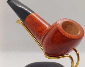 Pode incluir: Um cachimbo de madeira marrom com um bocal preto, apoiado em um suporte de metal dourado. O suporte está sobre uma base de pedra preta.