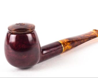 May include: A dark burgundy tobacco pipe with a smooth, rounded bowl and a matching lid. The stem features a marbled amber and brown pattern with a gold-coloured band connecting it to the bowl. The pipe has a polished finish throughout.